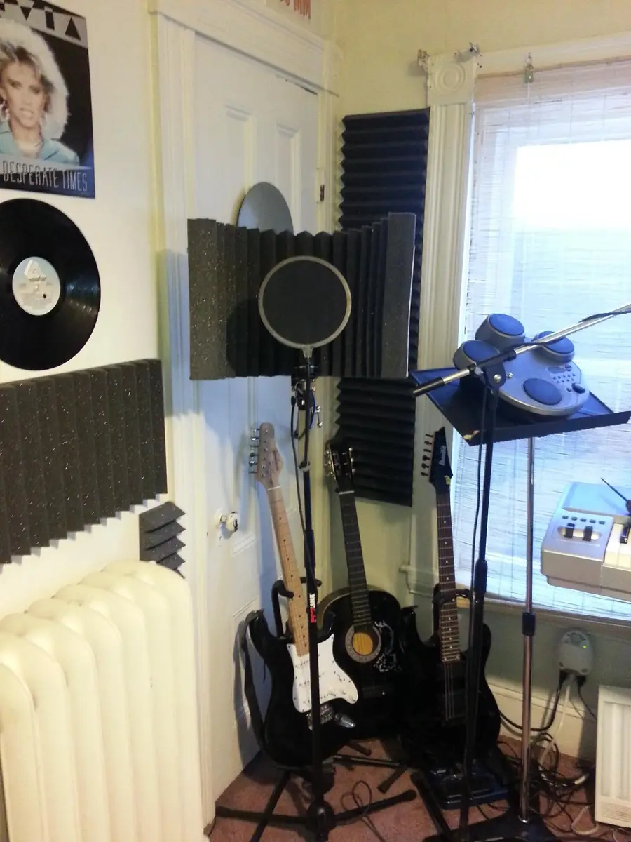 Recording corner with a microphone and pop filter, vinyl records and a portrait on the wall, guitars on stands and acoustic foam