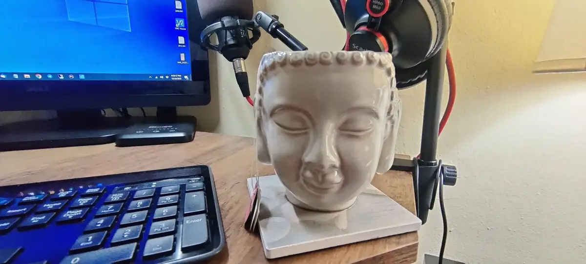 Desk with a white Buddha head, microphone on a boom arm and a monitor glowing blue