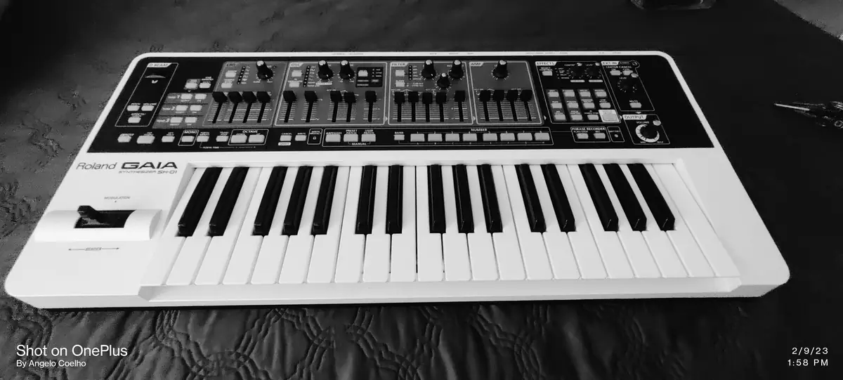 White keyboard synth with a dense black control panel of knobs, sliders and buttons on a dark backdrop