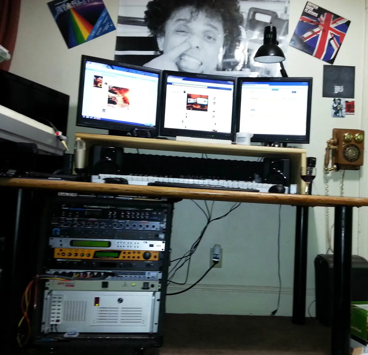 The first Crazy Chicken Studios setup in 2013: three monitors on a desk riser, a MIDI keyboard, a condenser mic and a rack of outboard audio gear under the desk, with rock posters on the wall