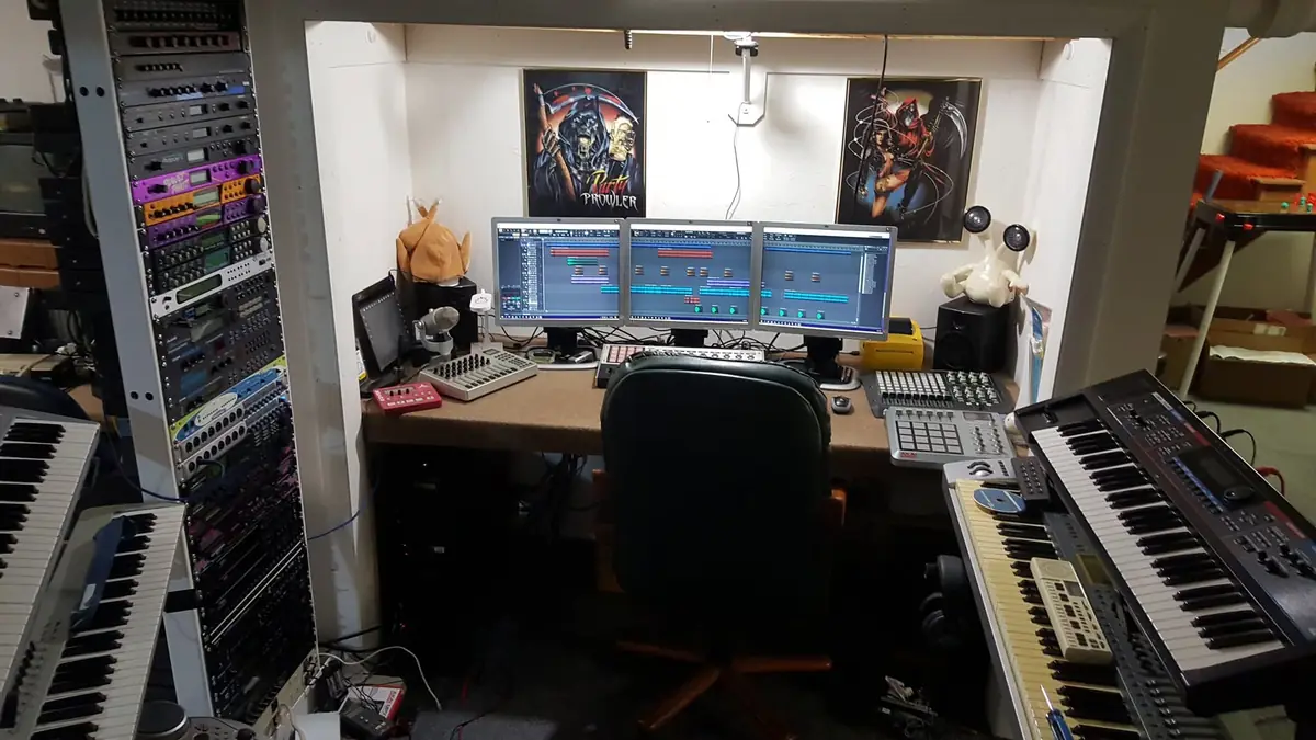 The second and most complete Crazy Chicken Studios setup around 2019: a triple-monitor DAW desk flanked by a fully loaded 19-inch outboard rack, multiple synthesizers and pad controllers