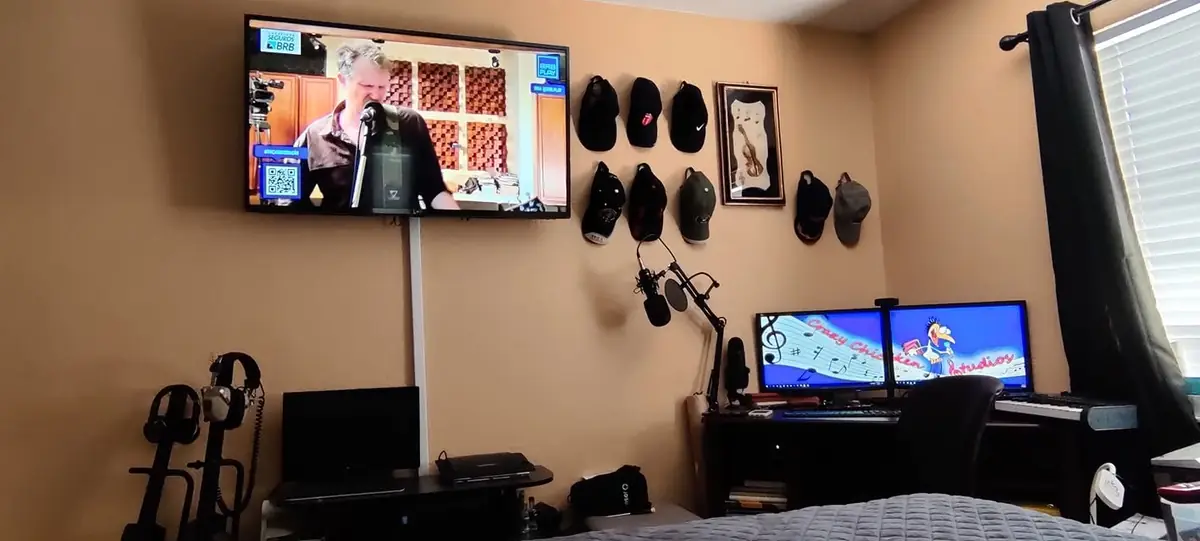 The third, heavily downsized studio setup around 2021: a compact bedroom corner with dual monitors, a wall-stowed microphone on a boom arm, headphones and a single MIDI keyboard